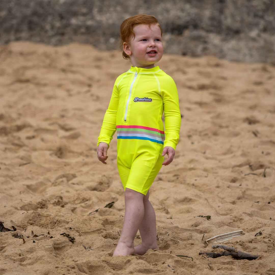 Baby in Shelly Beach yellow toddler swimsuit near shoreline