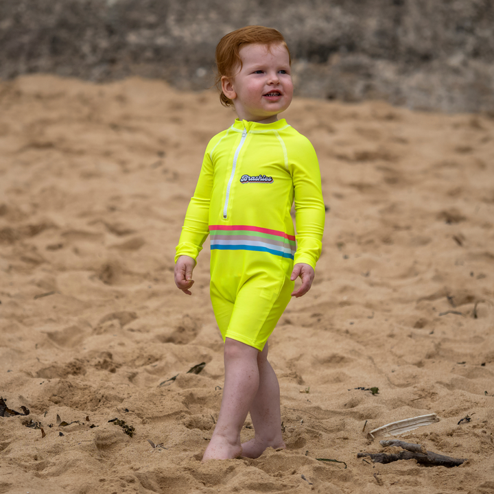 Baby in Shelly Beach yellow toddler swimsuit near shoreline