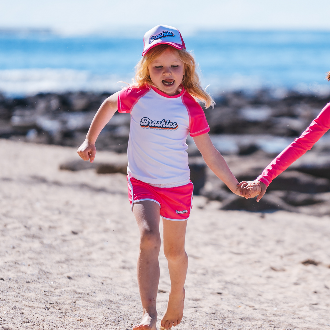 Girl wearing Avalon swim shorts in bright pink on the beach